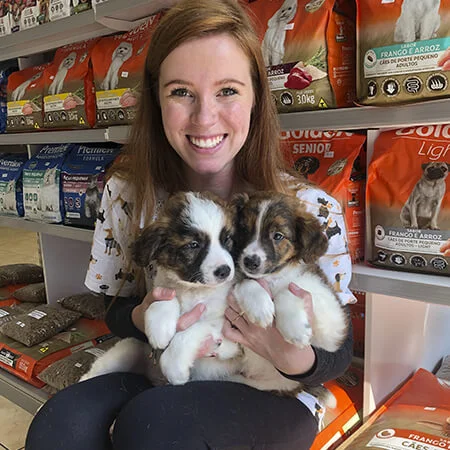 Veterinária abraçando dois cachorros, um com pelo branco e cinza e outro totalmente preto, demonstrando carinho e cuidado na clínica veterinária.