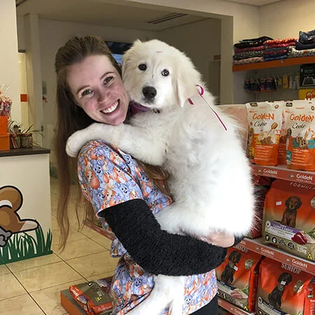 Dra. Fernanda, médica veterinária de Caxias do Sul, segurando um Pastor Samoieda branco no colo, enquanto veste um pijama cirúrgico decorado com cachorrinhos.